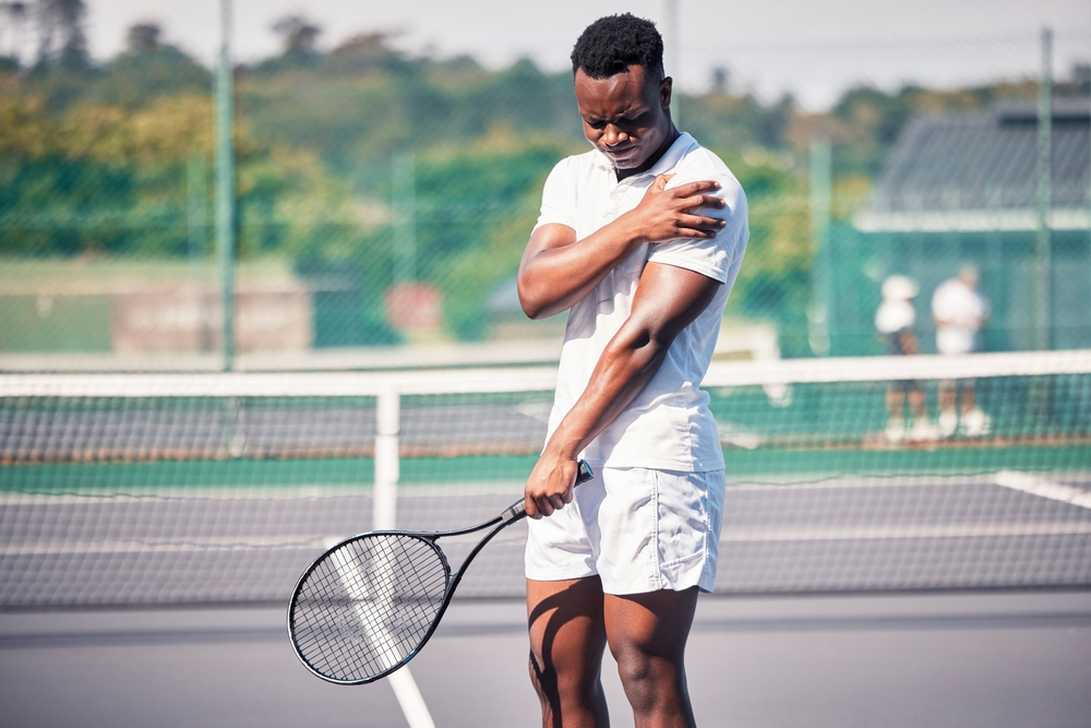 A man suffering from his arm in a tennis match - What Can Nola Stretch & Recovery Do to Improve Your Tennis Game