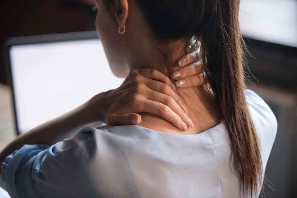 Woman massaging stiff neck and shoulder, experiencing pain from incorrect posture during computer work, concept of spinal erector discomfort