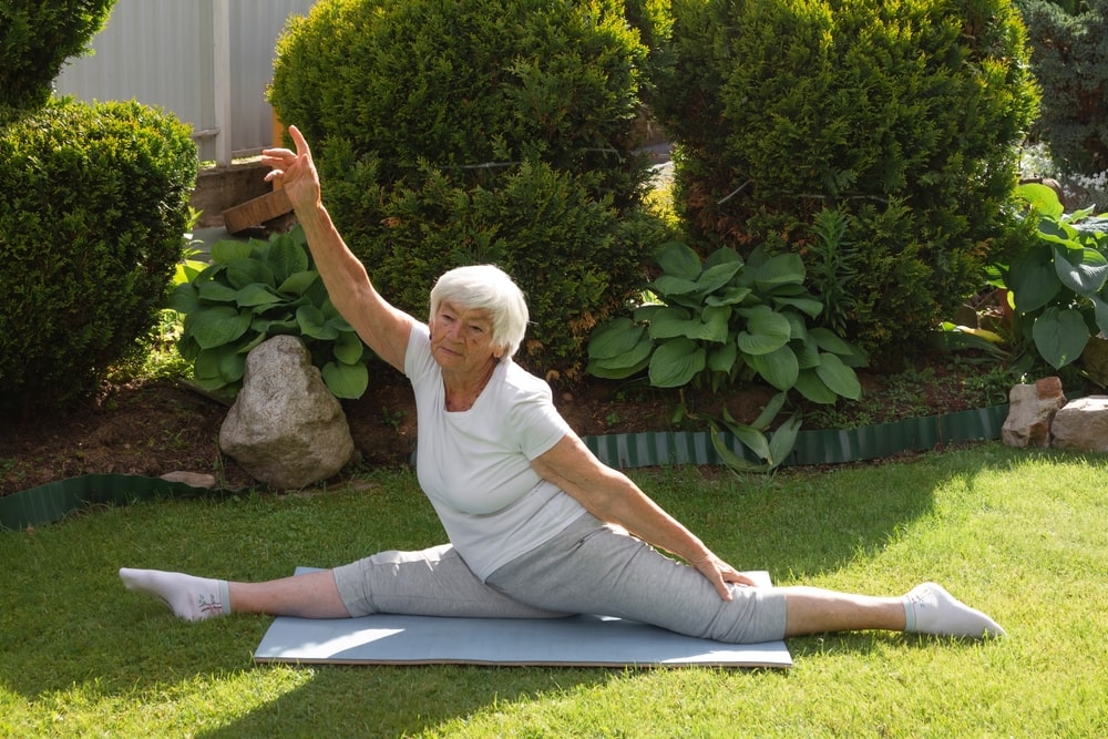 flexible old woman doing full split in a garden - reasons why you should try fascial stretch therapy in New orleans