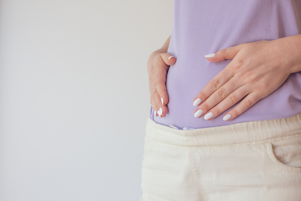 A pregnant woman standing, gently cradling her belly with her hands, showcasing the first and second trimesters of pregnancy in New Orleans.