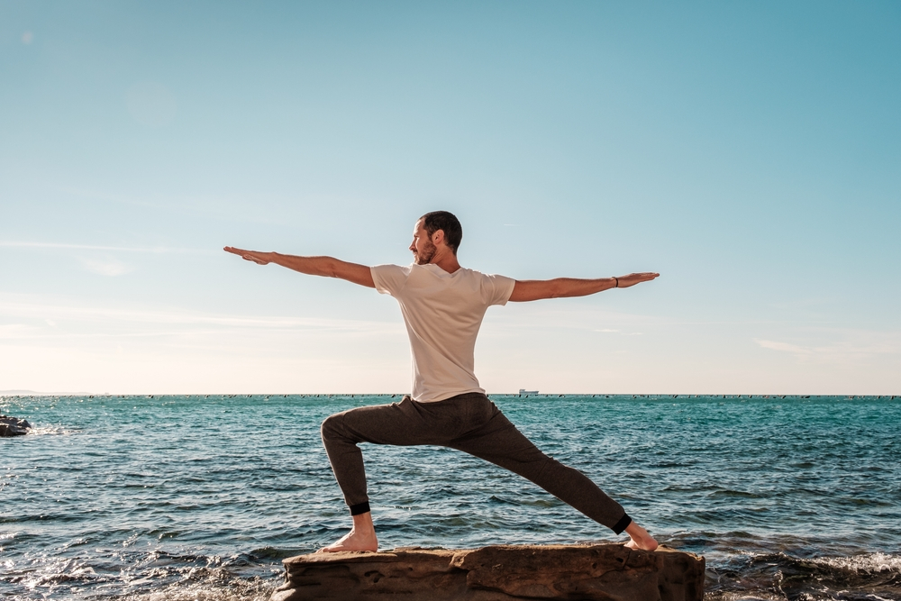 Young man engaging in Fascial Stretch Therapy outdoors, practicing yoga meditation and breathing exercises by the seaside.