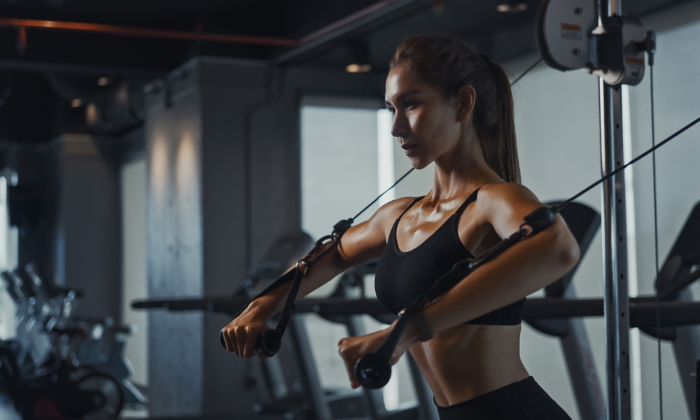 Athletic woman utilizing gym equipment for arm and shoulder exercises, embodying the strength and flexibility enhanced by Fascial Stretch Therapy.